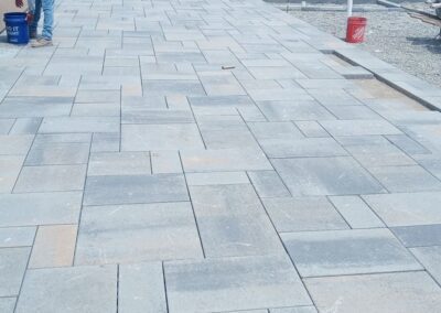 A walkway with grey pavers and a boat in the background.